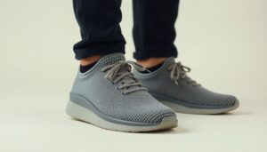 A person wearing dark pants and light grey Nexus Knit minimalist footwear by Xero Shoes with white soles, standing on a light surface. The shoes have laces and a textured pattern.